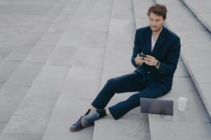 Man executive worker uses mobile phone for chatting works remotely makes project via laptop computer photo