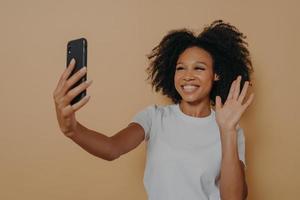 Cheerful african woman gesturing hi while making video call or taking selfie on smartphone photo