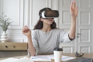 Concentrated woman bank accountant in VR headset sitting at desk at home office photo