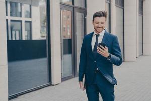 Confident happy young male business consultant holding modern smartphone and smiling outdoors photo