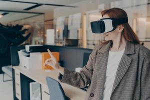 Smiling happy businesswoman wearing VR headset trying out virtual reality for first time at work photo