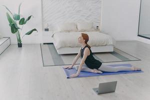 joven y bonita deportista practicando yoga frente a la computadora. asanas de estiramiento. rutina de la mañana. foto