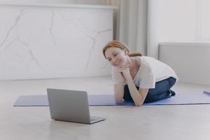 una mujer blanca sonriente tiene entrenamiento personal remoto y habla frente a la computadora. foto