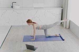 Teacher shows workout on the online lesson. Young adult european woman is doing plank exercise photo