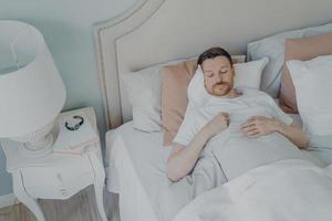 apuesto joven barbudo durmiendo en una cama espaciosa y cómoda foto