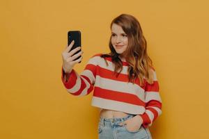 joven bloguera encantadora hablando selfie en teléfono móvil mientras posa sobre fondo amarillo foto