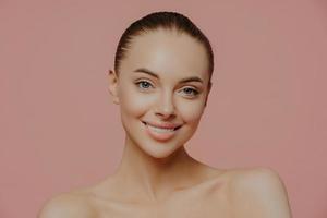 Shirtless beautiful young female model with makeup and clean fresh skin, cares about complexion, smiles gently and looks directly at camera, isolated. Cosmetology, spa, facial treatment concept photo