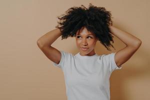 Young attractive sensual african woman touching with hands curly hair, isolated on beige background photo