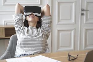 Young happy female employee in VR goggles at workplace watching movies photo