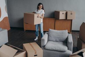 Hispanic girl is holding box and leaving apartment. Happy young woman relocates alone. photo