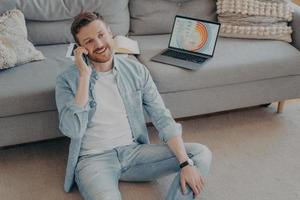 Young man working remotely from home calling project partner photo