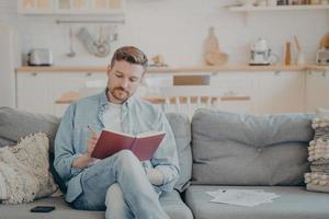 joven escribiendo en un cuaderno mientras se sienta en el sofá foto