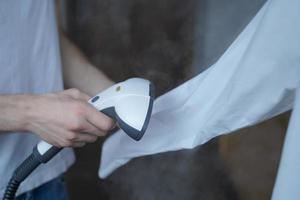 foto recortada de un hombre que usa un vaporizador que plancha cuidadosamente una camisa blanca mientras sostiene una manga larga