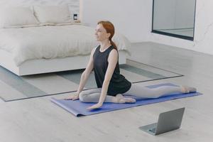 Young caucasian woman stretching and doing morning exercises. Home isolation and internet learning. photo
