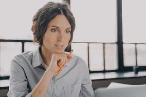 Pensive young hispanic business woman looking at laptop screen, using modern technology at work photo