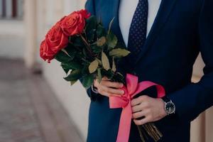 Man dressed in blue suit holding bouquet of red roses photo