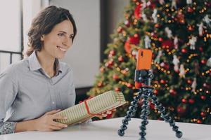 Smiling positive female blogger recording video tutorial about tips for wrapping Christmas presents photo