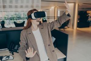 Woman wearing VR headset surprised with virtual reality while standing near her workplace in office photo