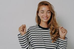 Young excited woman clenching fists for good luck with closed eyes and smile waiting for fortune photo