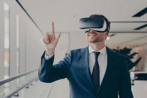 Cheerful businessman dressed formally using vr headset at work photo