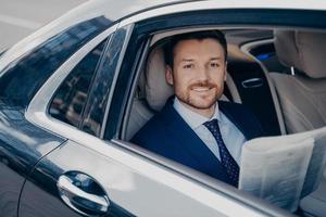 joven empresario con estilo lee el periódico en el asiento trasero del coche foto