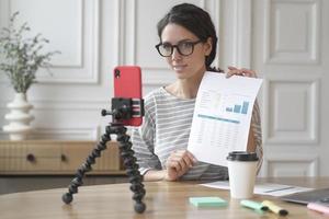 Positive couch lady records video at home, streaming online podcast on mobile phone on tripod photo