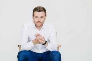 Indoor portrait of handsome self confident businessman in white shirt and black trousers, looks with serious expression, ready to have business meeting with colleagues, isolated over white studio photo