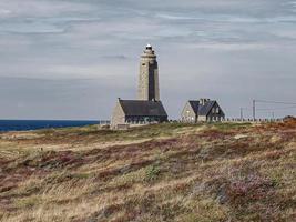 Lighthouse in meadow on coast by sea photo