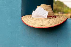 sombrero de bambú tejido del granjero con una máscara en un muro de hormigón azul. foto