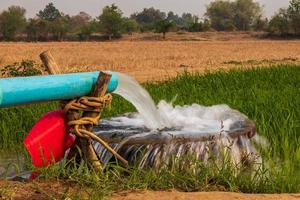 Water flows from pipes into a basin in rice fields near arid soil. photo