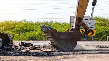 Backhoe shovel demolishing asphalt road. photo