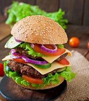 Gran jugosa hamburguesa con verduras y carne sobre un fondo de madera en estilo rústico foto