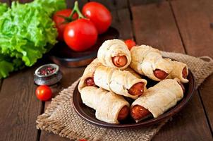 Sausage in the dough sprinkled with sesame seeds on a wooden background in rustic style photo