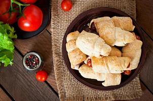 Sausage in the dough sprinkled with sesame seeds on a wooden background in rustic style photo