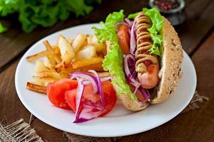 Perrito caliente con salsa de tomate mostaza y lechuga sobre fondo de madera. foto