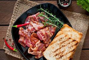 Fried bacon and toast on a black plate on a wooden background photo