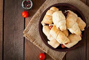 Sausage in the dough sprinkled with sesame seeds on a wooden background in rustic style photo