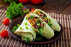 Burritos wraps with minced beef and vegetables on a wooden background photo