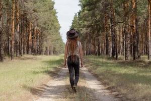 young woman with dreadlocks walking on the road, big pines background, girl hiker in woods photo