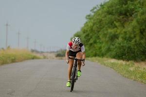 Bicycle racer in helmet and sportswear training alone on empty country road, fields and trees background