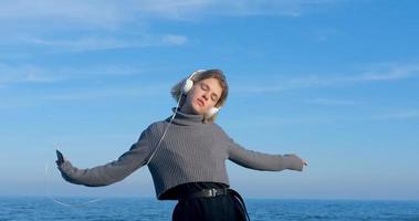 Una joven y guapa mujer escucha música con auriculares al aire libre en la playa contra el cielo azul soleado foto
