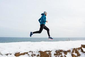 joven corredor masculino entrenando al aire libre en invierno, el hombre corre en la nieve foto