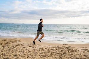 ajuste el entrenamiento de corredores masculinos en la playa de verano y escuche música contra el hermoso cielo y el mar foto