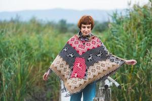 Young woman traveler dressed in a poncho walk outdoors in autumn fields photo