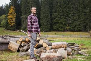 yong male in forest choping wood with steel axe, country landscape with lumberjack photo