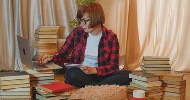 Young woman student studying at home with many books and laptop video