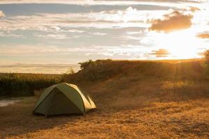 carpa verde de excursionistas cerca del río durante el atardecer o el amanecer foto