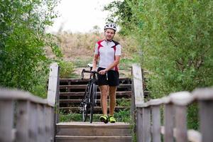 ciclista profesional en uniforme y casco en el viejo puente de madera, fondo del campo foto