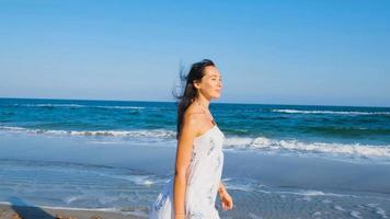 Young beautiful woman dressed in a white dress walk barefoot on the summer beach photo