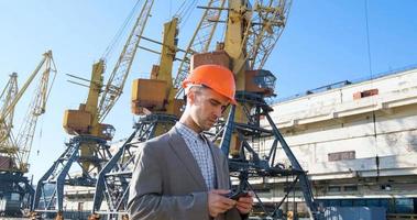 Young male worker of sea harbor in helmet, cargo manager in suit and halmet works outdoor , cranes and sea background